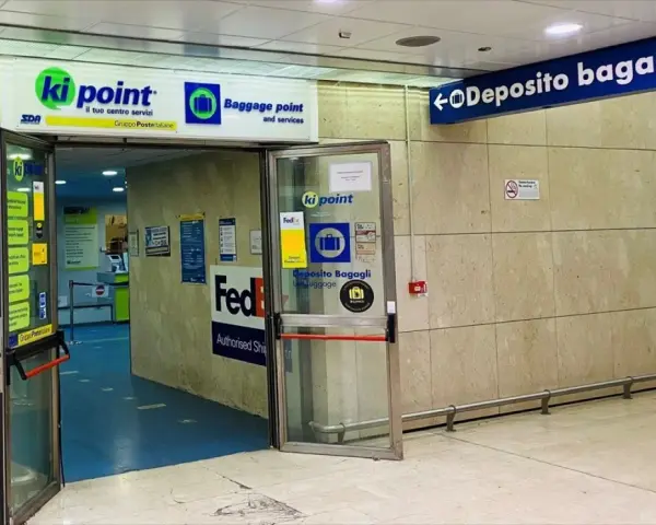 Entrance to a Ki Point baggage storage facility with signage for "Deposito Bagagli" and FedEx.