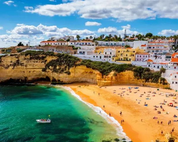 Coastal town with white buildings on cliffs overlooking a sandy beach and turquoise water.