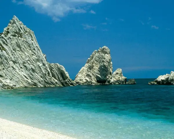 White pebble beach with turquoise water and dramatic white rock formations under a clear blue sky.